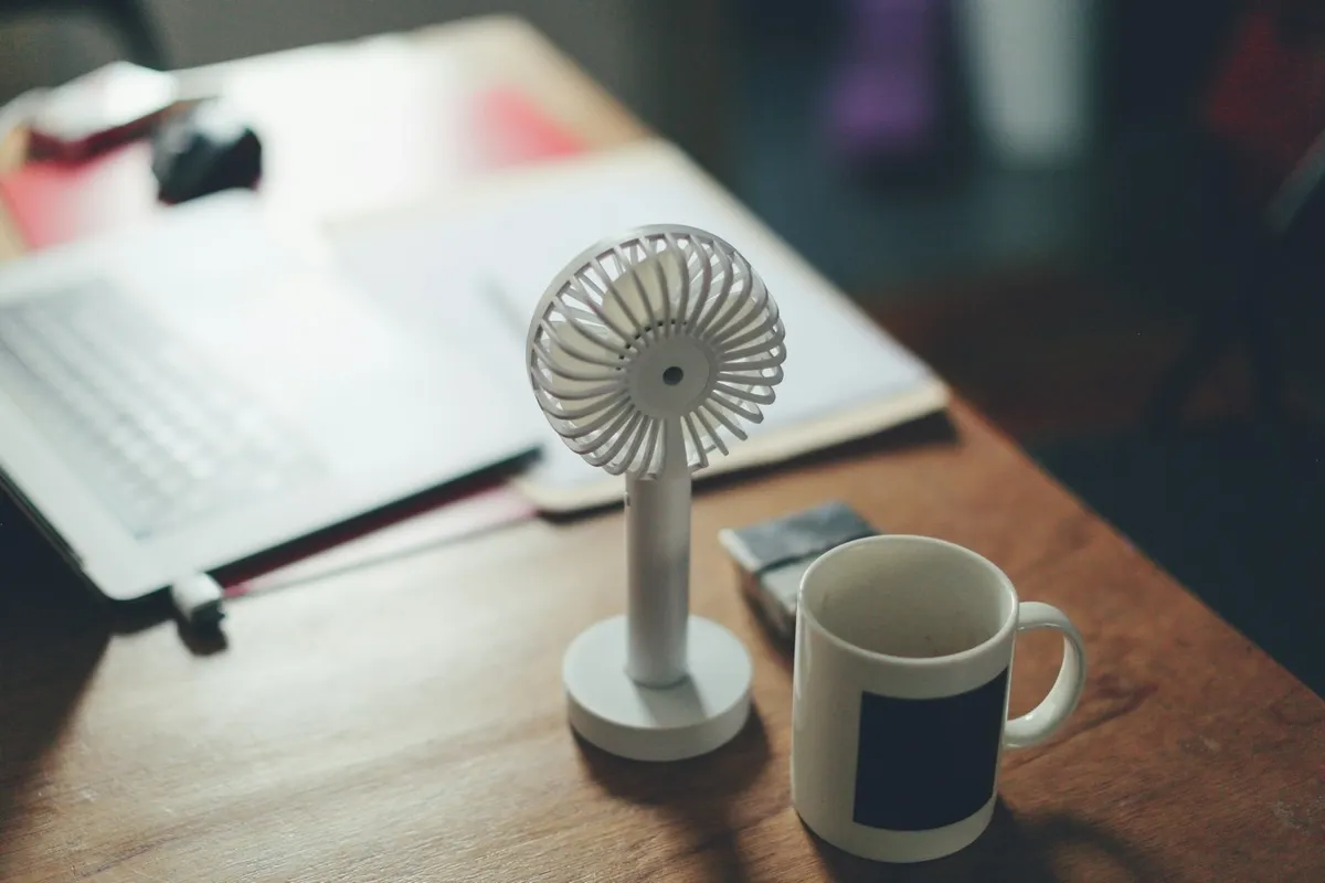 Petit ventilateur de bureau et mug posés près d'un ordinateur portable pendant une vague de chaleur