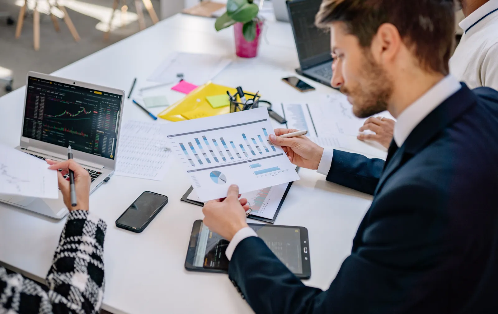 Deux collaborateurs analysent ensemble des graphiques imprimés et des relevés de données sur un bureau, à côté d'un ordinateur portable
