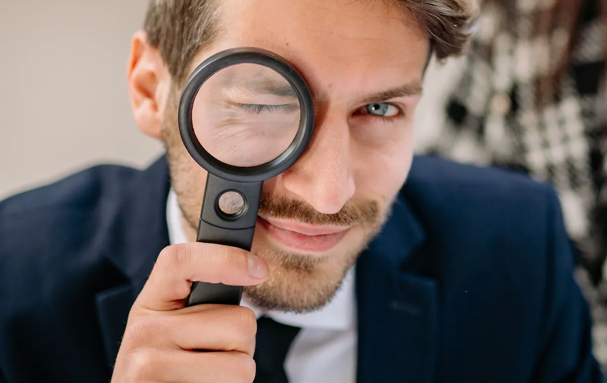 Homme en costume observant à travers une loupe, son œil grossi par la lentille