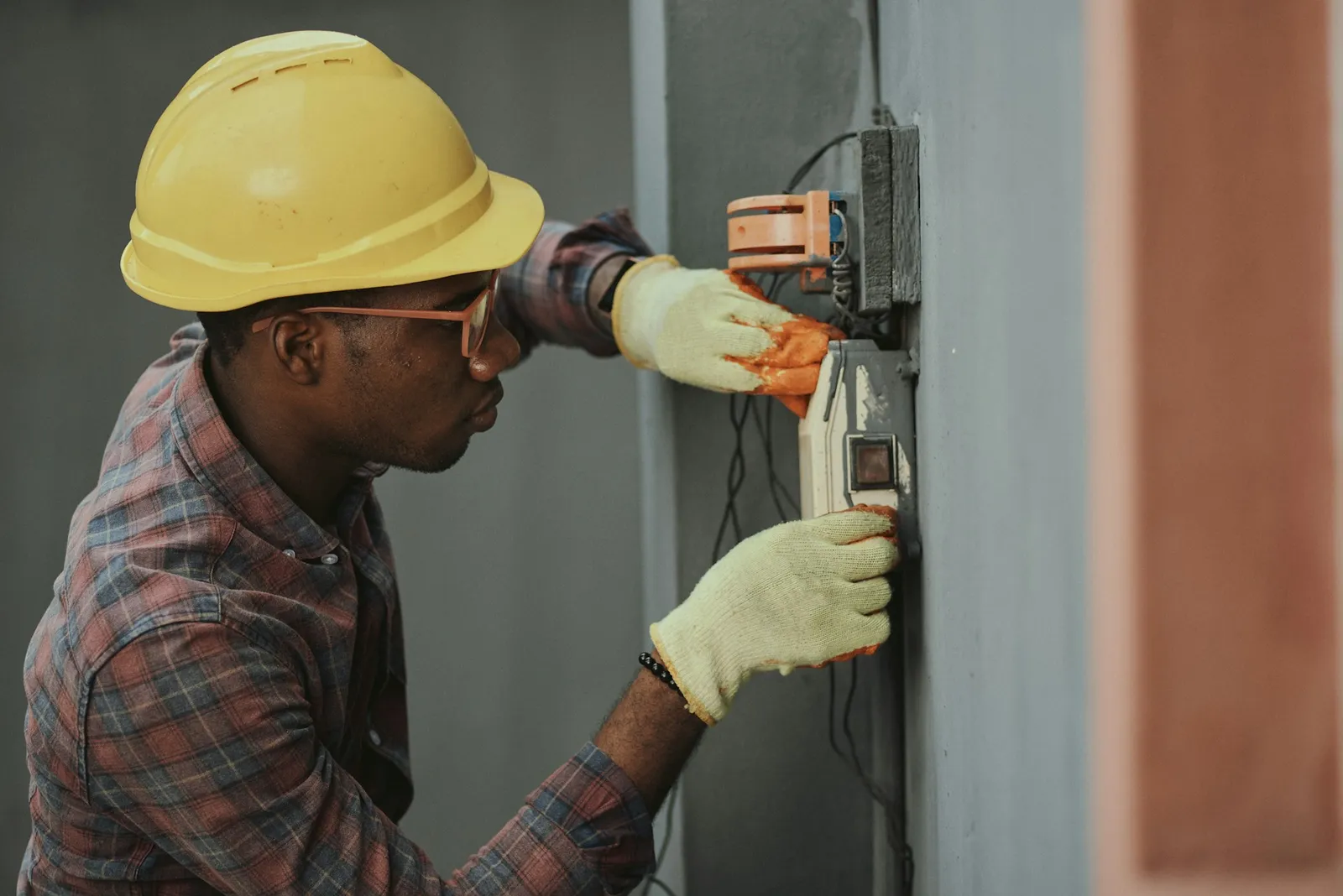 Un technicien casqué et ganté intervient sur un boîtier électrique fixé au mur d'un bâtiment tertiaire