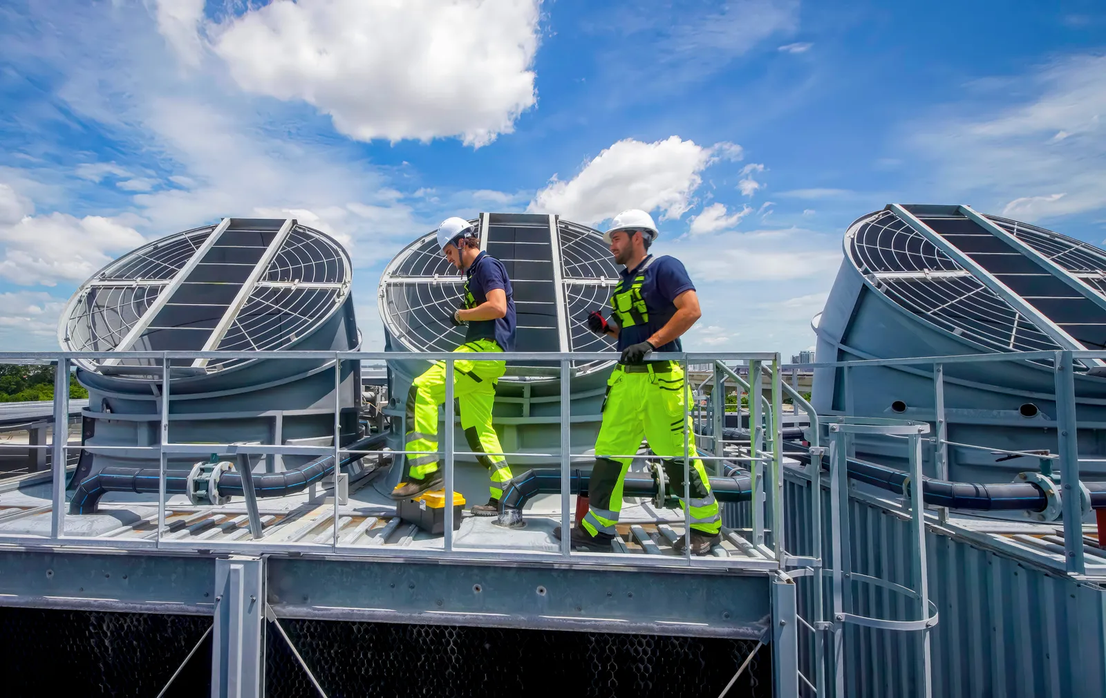 Deux techniciens de maintenance en tenue de sécurité interviennent sur des groupes froids installés en toiture d'un immeuble tertiaire