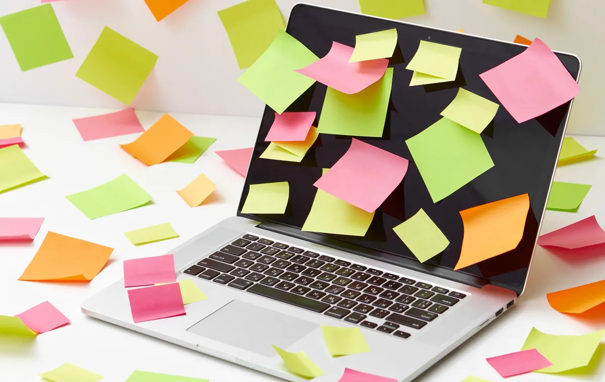 Un ordinateur portable entièrement recouvert de post-it multicolores, éparpillés jusque sur le bureau