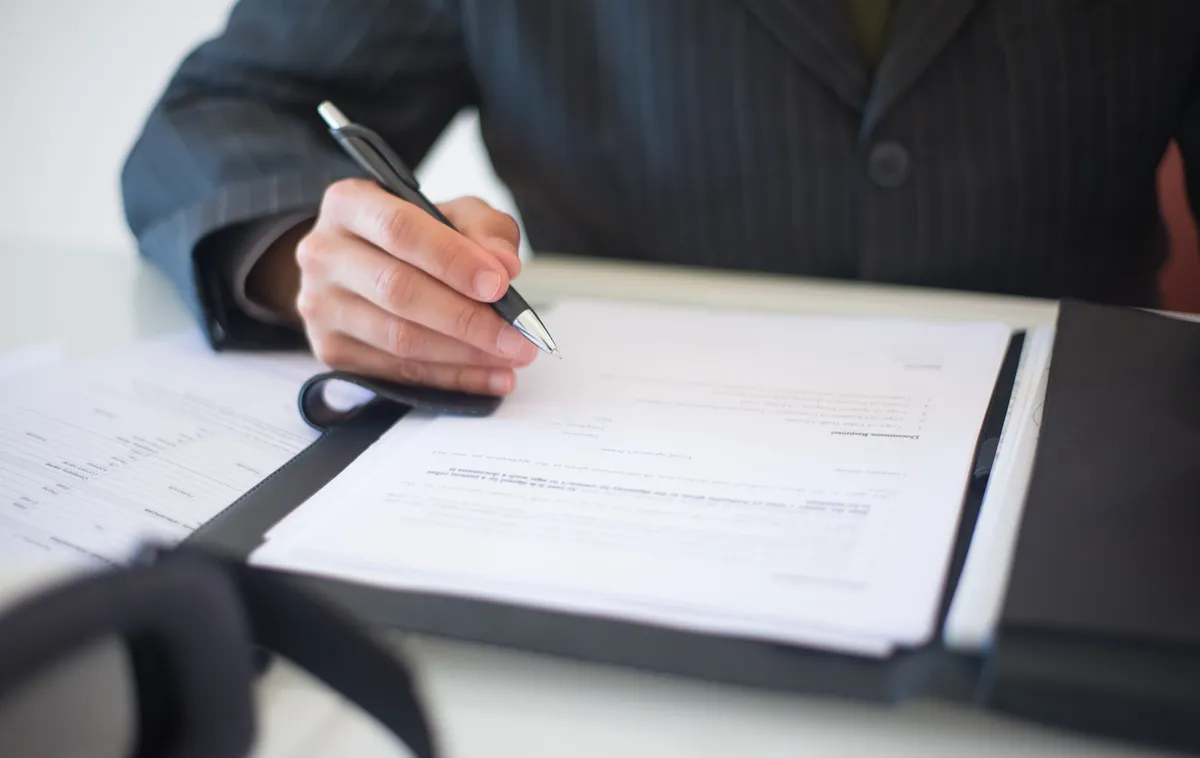 Gros plan sur une main qui remplit et signe un document d’évaluation des risques professionnels posé sur un bureau