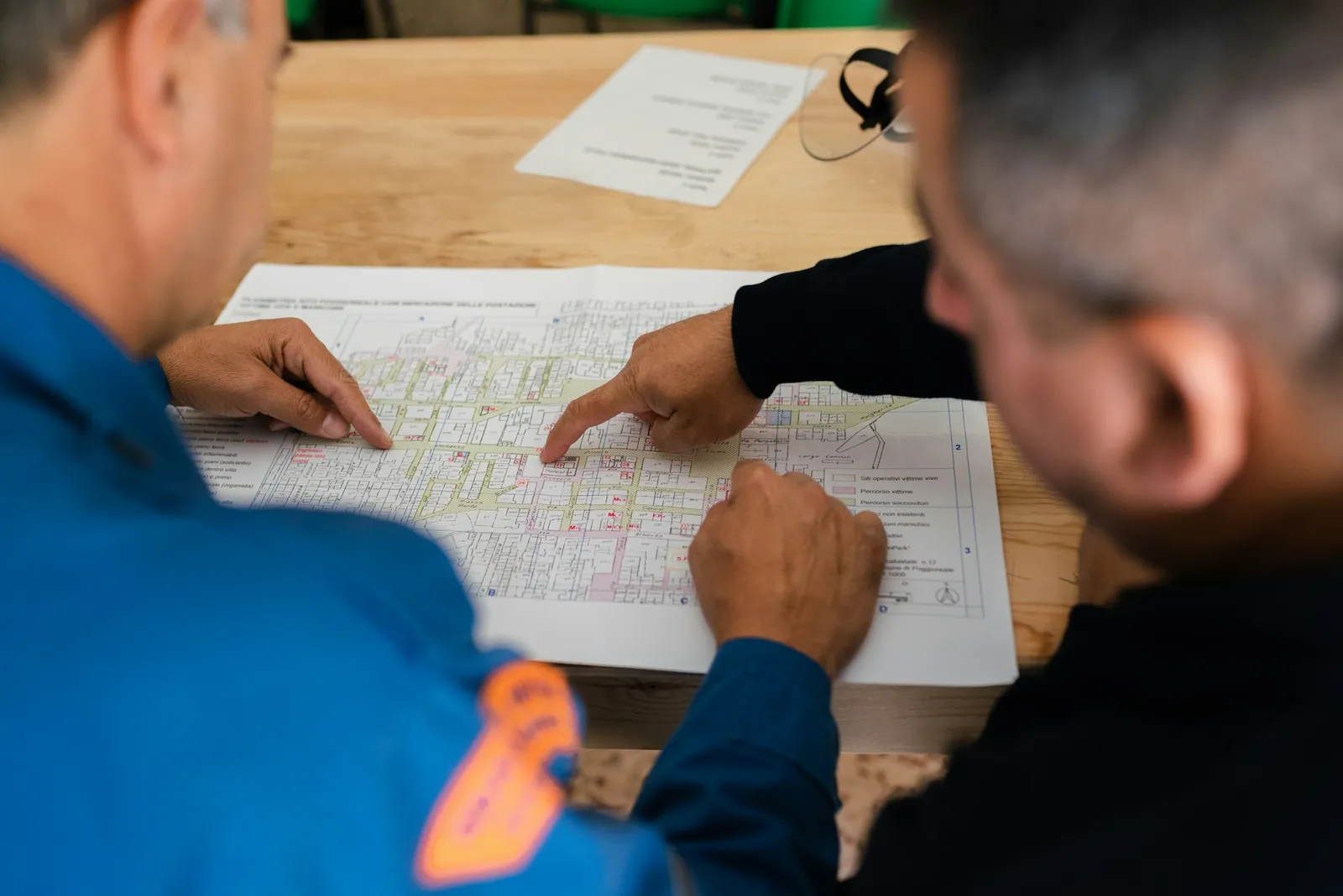 Deux hommes penchés sur un plan de bâtiment déplié sur une table, l'un d'eux pointant du doigt une zone du plan