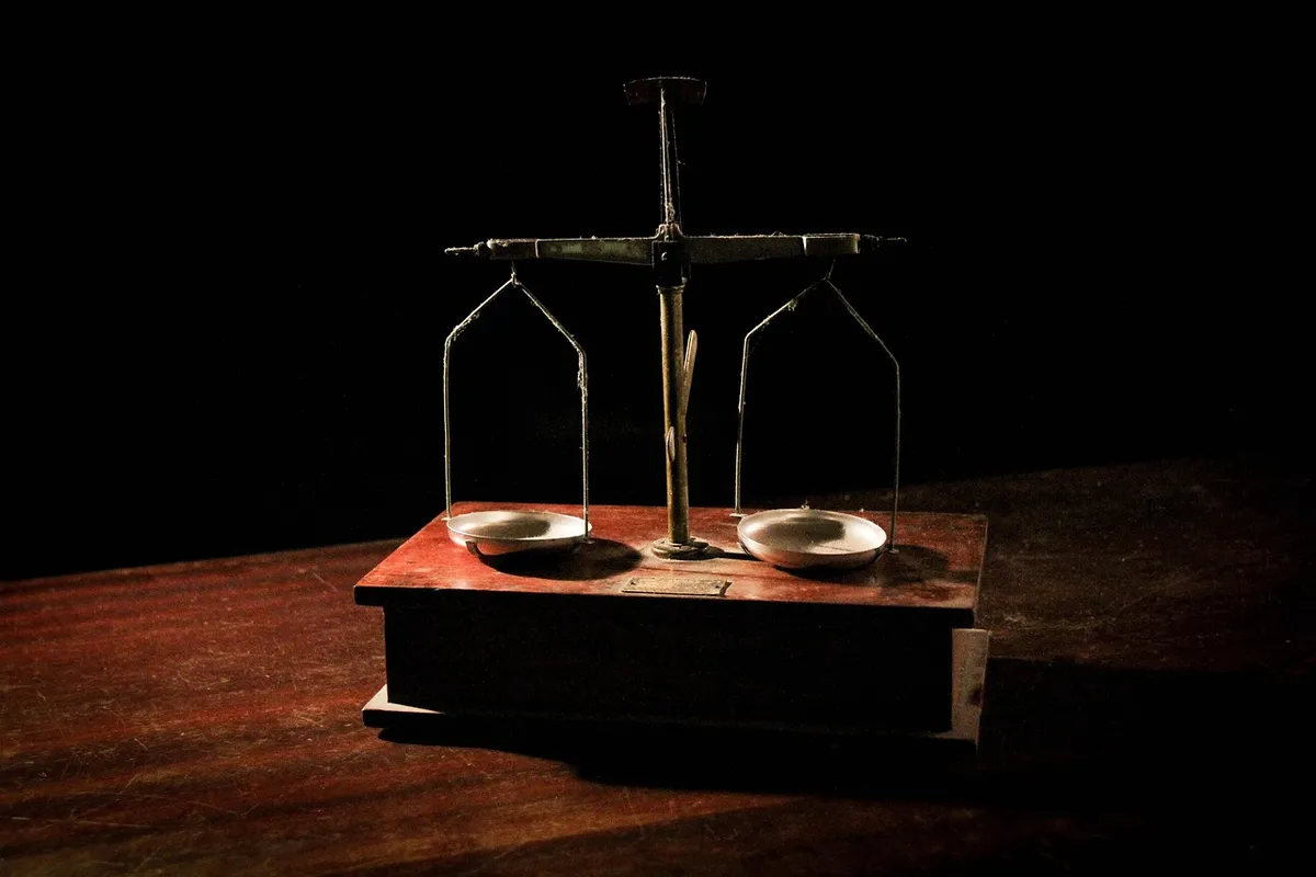Une balance à deux plateaux posée sur une table en bois, éclairée dans la pénombre