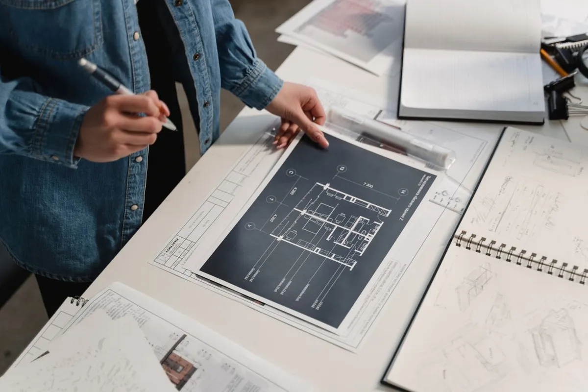 Une personne annote un plan d'aménagement de bureaux posé sur une table de travail, entouré de croquis