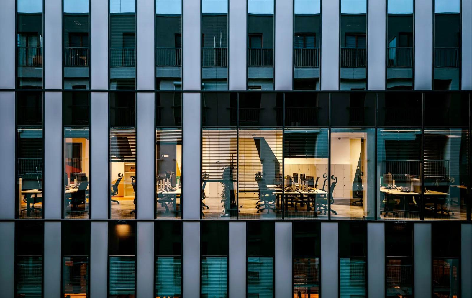 Façade vitrée d'un immeuble de bureaux en soirée : certains plateaux sont éclairés et occupés, d'autres restent dans le noir
