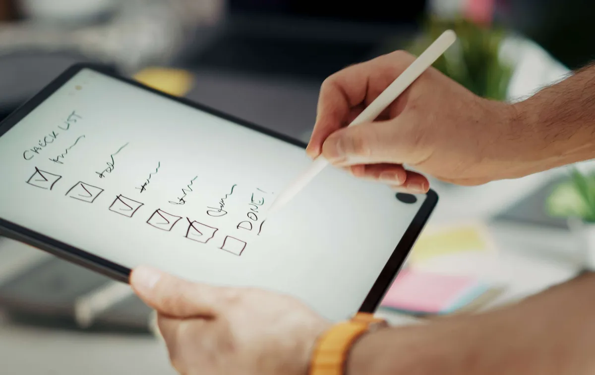 Main cochant une check-list sur une tablette avec un stylet, illustration d'un playbook d'urgence