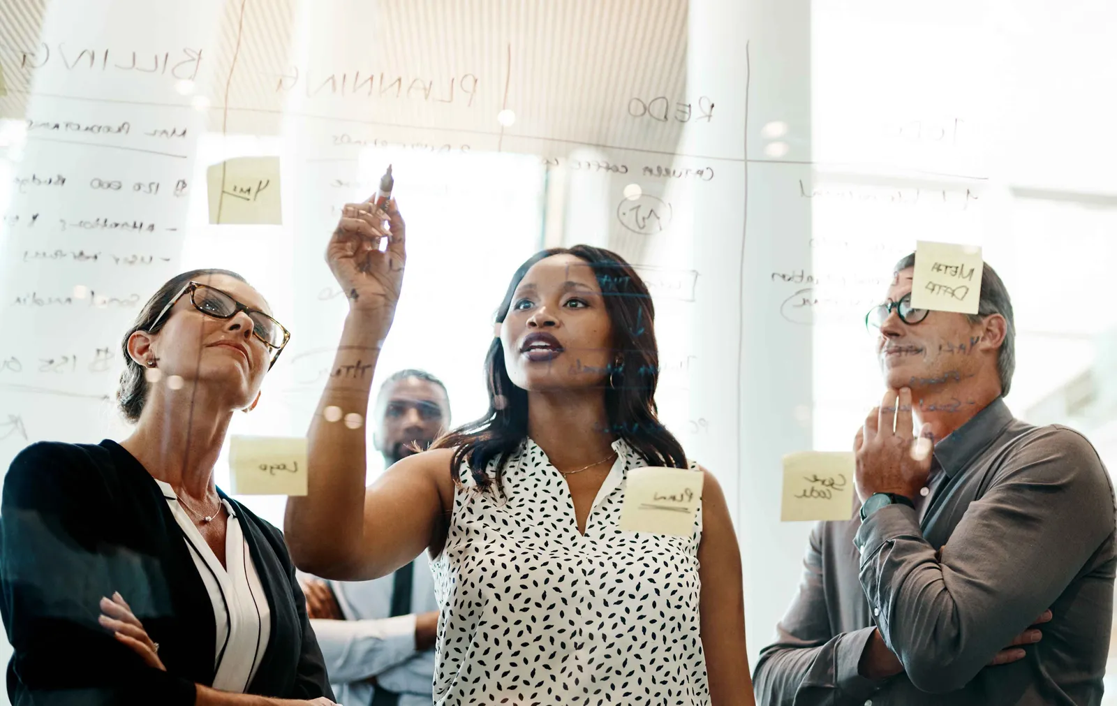 Trois collaborateurs planifient ensemble devant un tableau vitré couvert de post-it